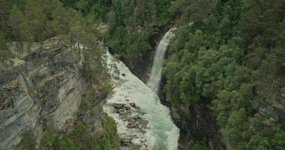 Aerial waterfall flowing rapidly into raging river through the canyon