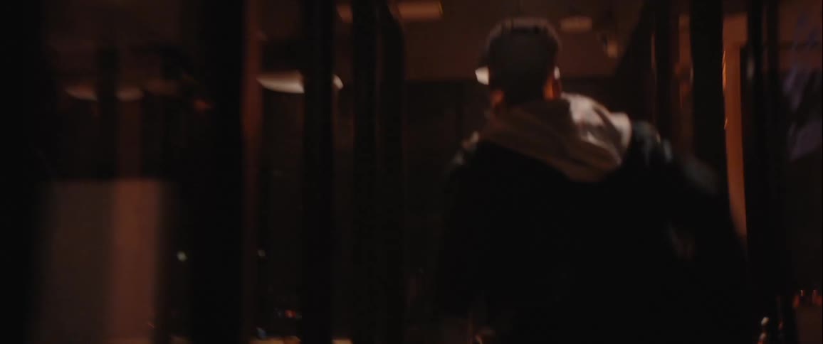 The man is running away looking back over his shoulder in a dimly lit corridor