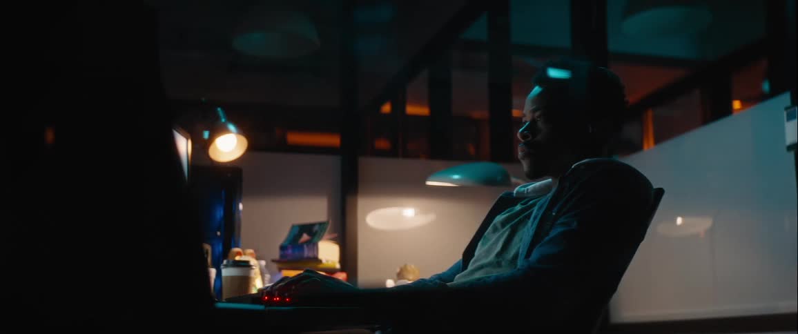 Man sitting at an office desk at night interacting with a computer