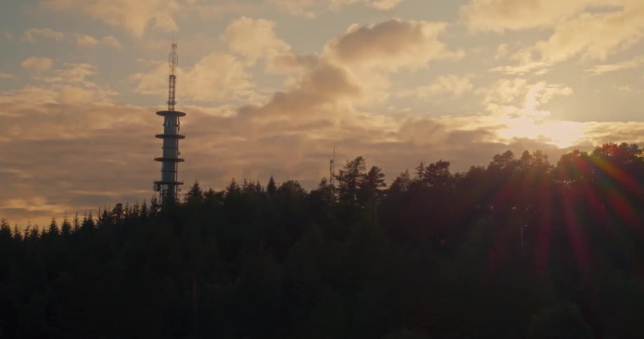 Silhouette of a mountain with conifers and an imposing antenna with the sun on the horizon