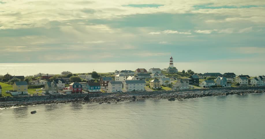 Aerial of a coastal village and a lighthouse on a partly cloudy summer day