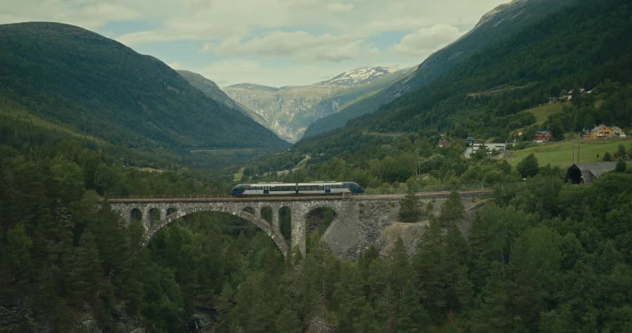 A sleek train glides across a historic stone bridge surrounded by lush green mountains and a breathtaking valley