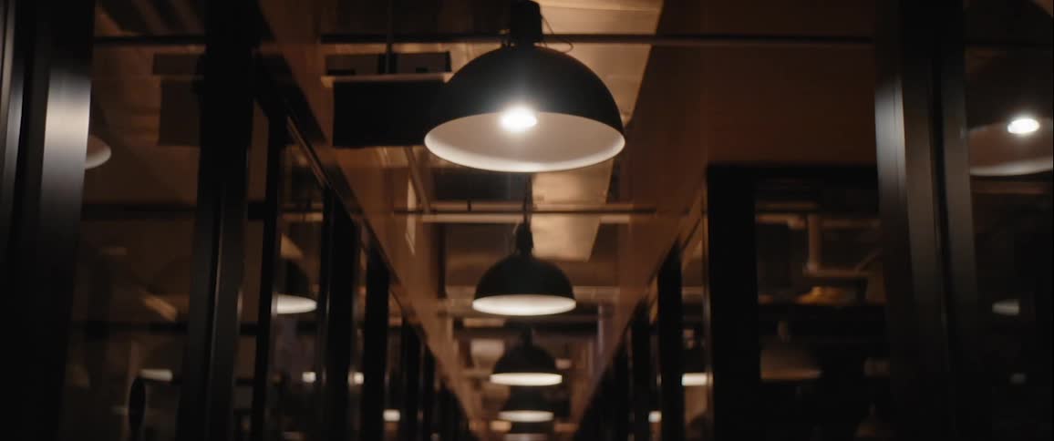 A dimly lit narrow passage or corridor with hanging light fixtures where the lights are in the process of being turned on creating a sense of depth and perspective