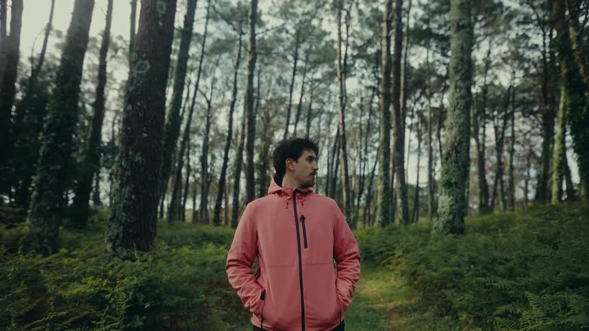 Man in orange jacket standing in middle of forest looking around