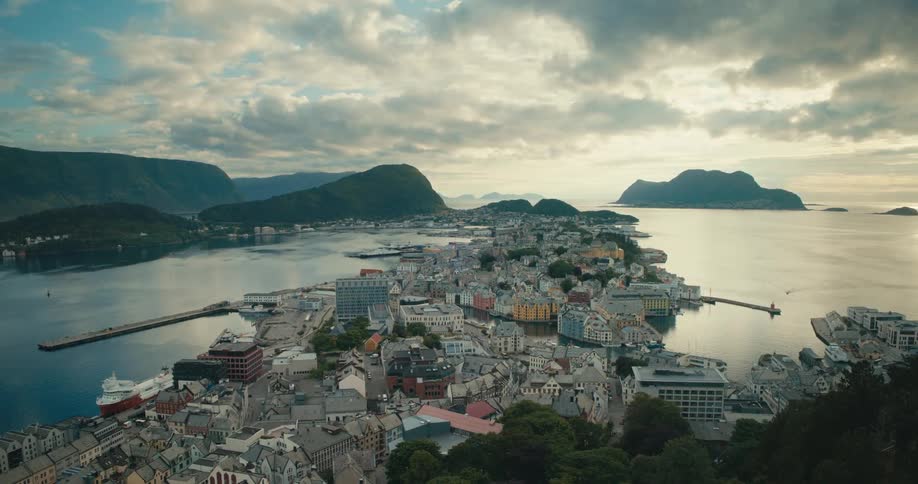 An aerial view of Aalesund norway showcasing the citys unique architecture harbor and surrounding mountains and fjords under a partly cloudy sky