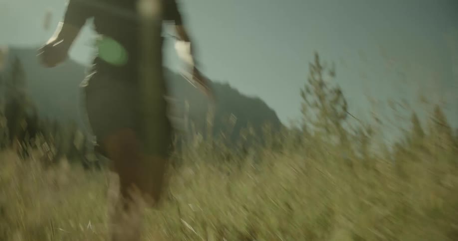A runner moves swiftly through a sunlit grassy field with a mountain and trees in the background capturing a moment of energy and adventure in nature