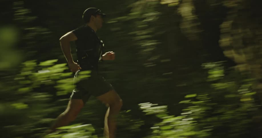 A man wearing a black cap shirt and shorts jogs in the forest