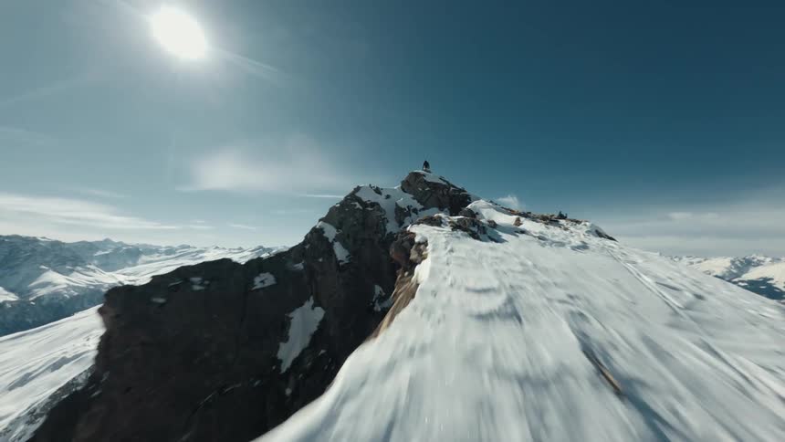 Aerial of a mountain climber standing on a summit on a mostly sunny winter day