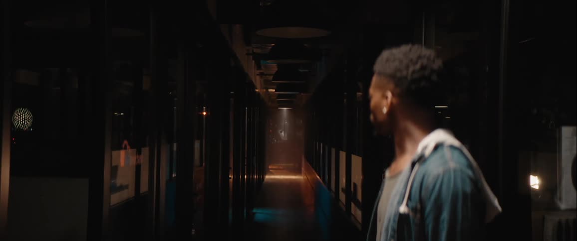 A man walking through a building at night notices a light turned on at the other end of a long hallway