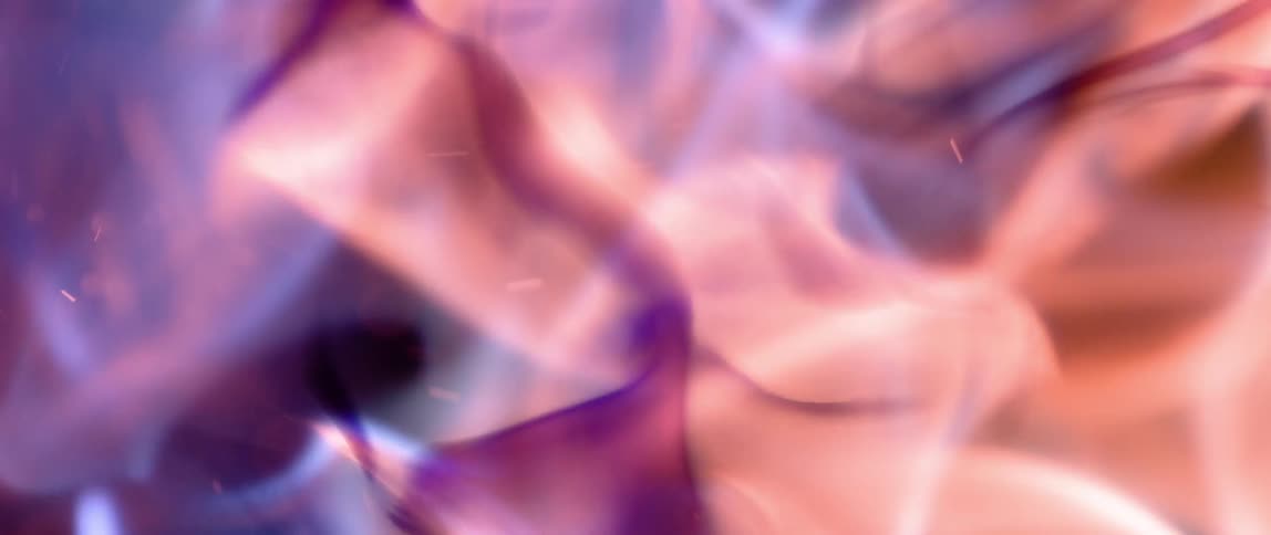 An orange and purple flame burns slowly as white smoke streaks peek through