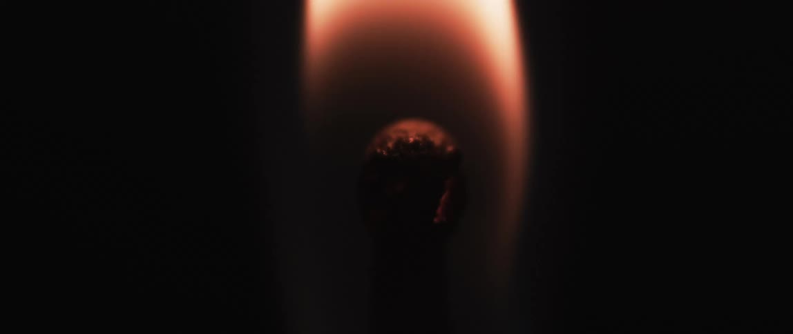 A burning match head against a dark background