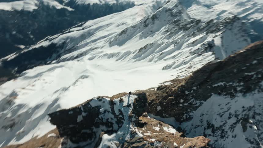 A lone adventurer stands on the edge of a snowy mountain peak gazing at the vast rugged landscape below