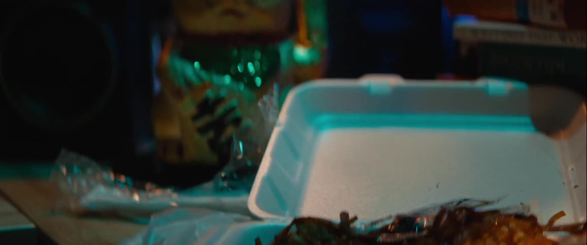 Food in a styrofoam box with a plastic fork on a table next to a ceramic asian lucky cat