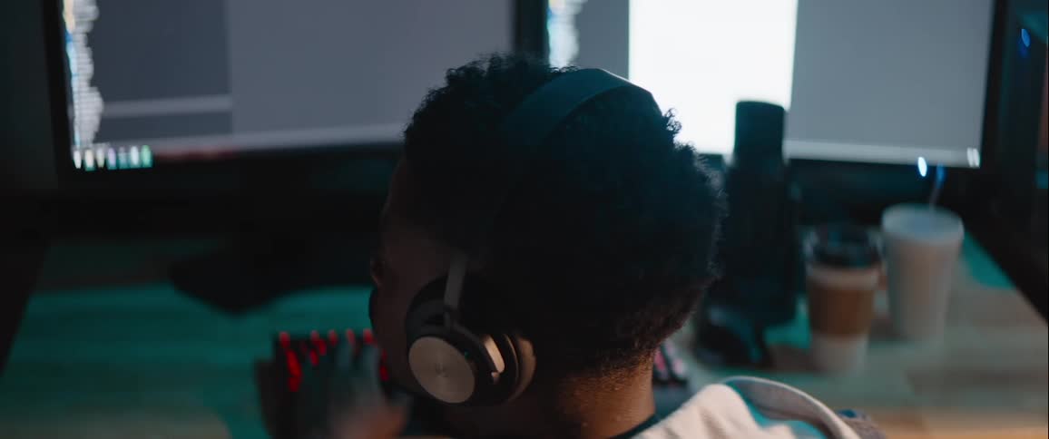 Man wearing headphones while working on a computer takes his headphones off to listen for a sound