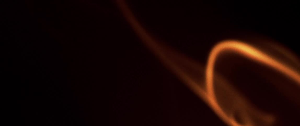 A closeup shot focuses on smoke delicately rising upwards bathed in a warm and vibrant orange light that beautifully illuminates its wispy form against the dark background