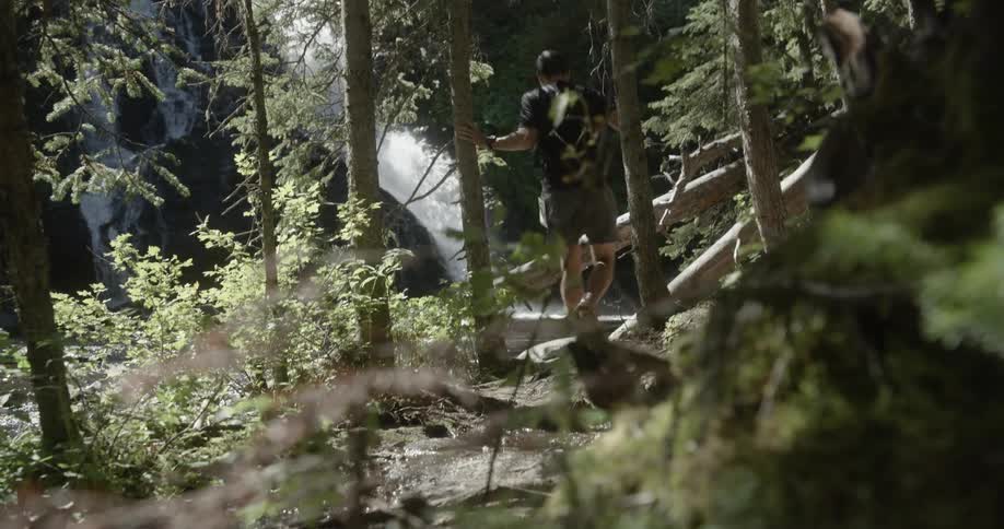 Man runs along a trail through the woods that leads towards a waterfall