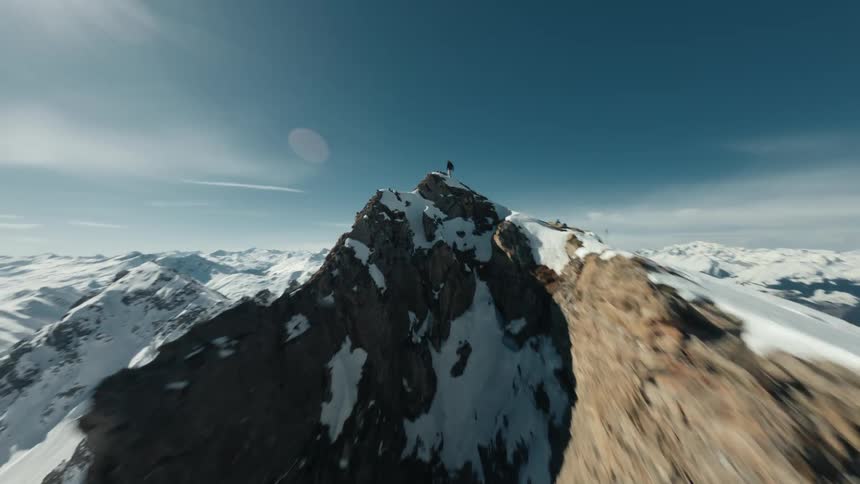 Aerial of a mountain climber standing on a mountain peak on a mostly sunny winter day
