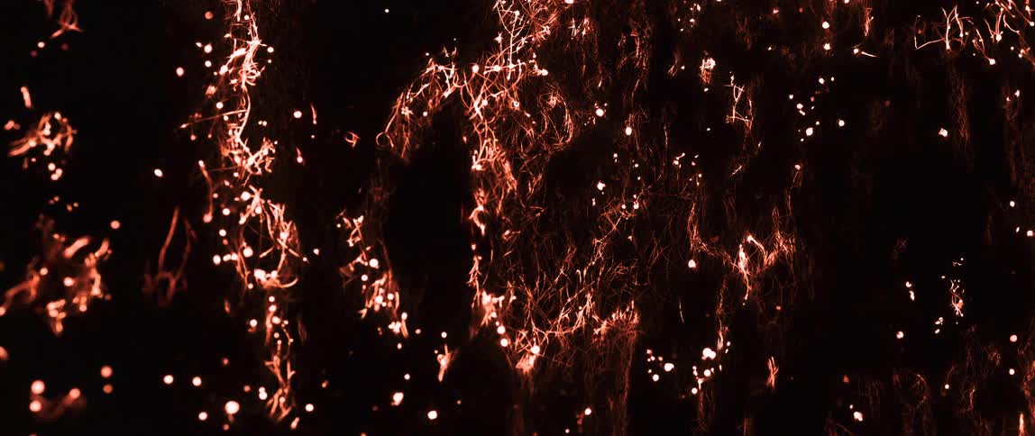 A closeup of strands of fiber burning without flames over a dark background