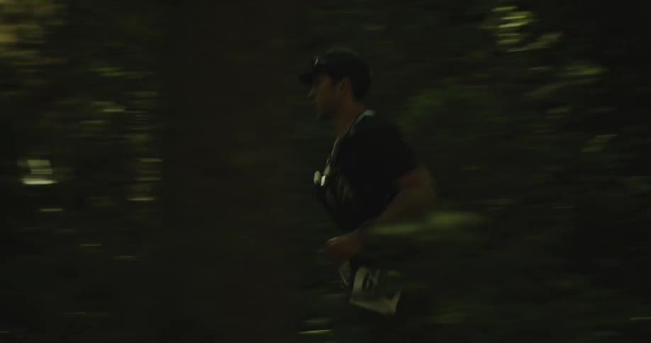 Man in cap and numeral running on a trail in the forest