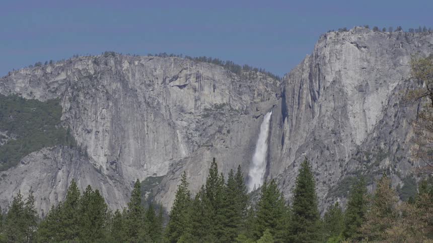 A waterfall flows from a mountain on a sunny day