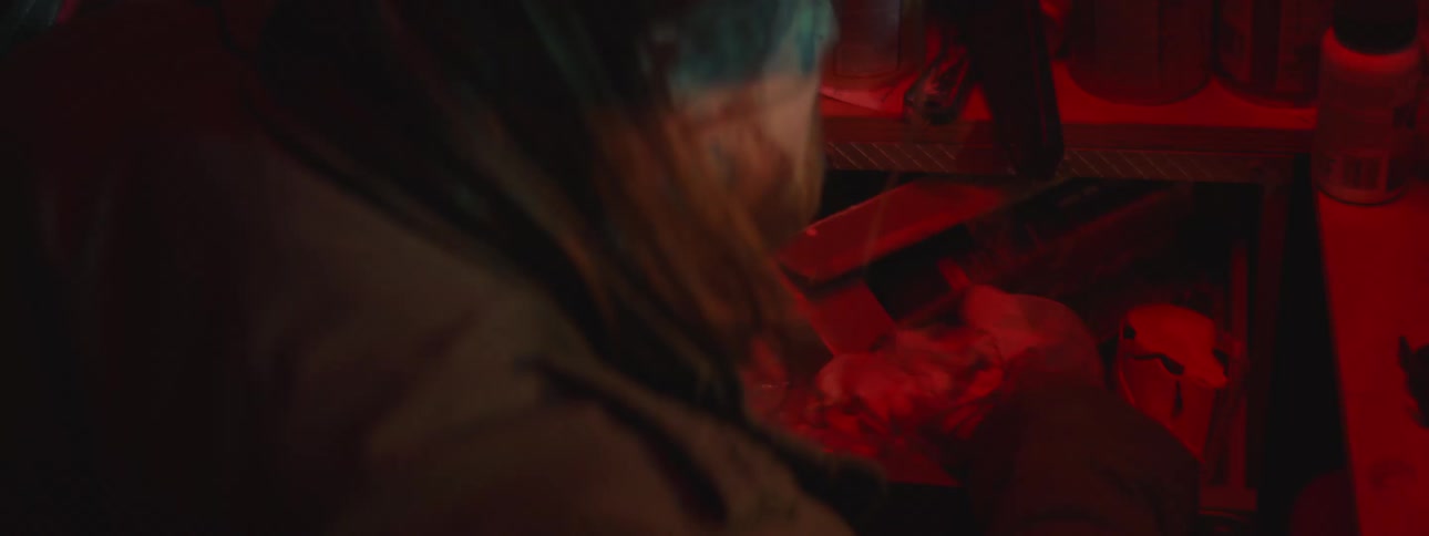 A person with a tattoo on their hand opens a cluttered drawer illuminated by red light and rummages through its contents