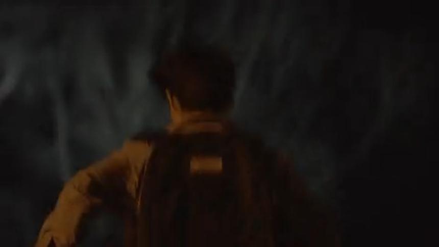 A person wearing a backpack runs through a dark blurry outdoor environment possibly a wooded area at night