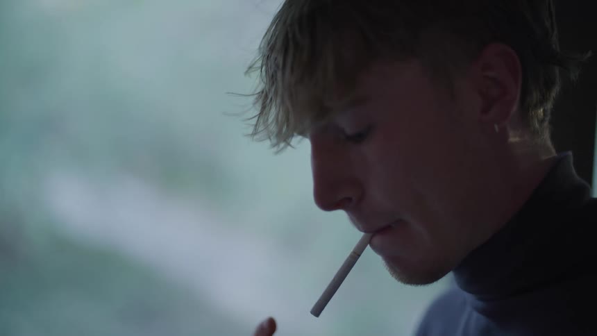 Man in profile holds a cigarette between his lips as he lights it
