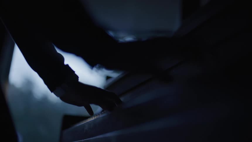 Silhouette of a persons hands playing the piano in a dimly lit environment