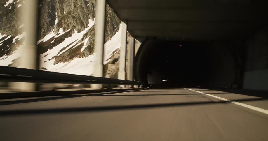 A person on a motorcycle rides out of a tunnel in a mountain