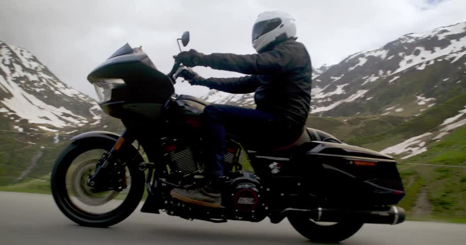 Motorcyclist in a white helmet and black clothes rides a black touring motorcycle along a road surrounded by snowy mountains