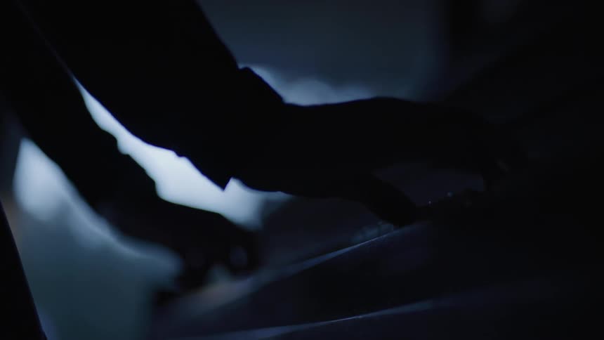 A musicians silhouetted hands play a piano in a dimly lit scene