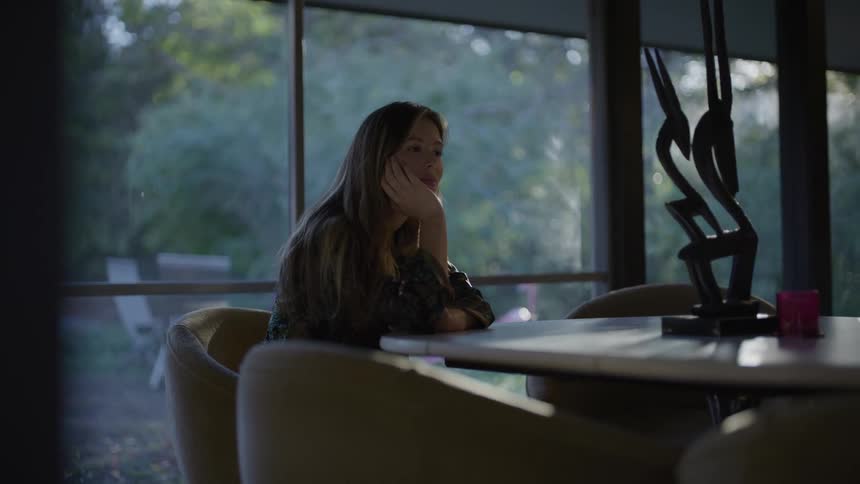 A woman sits at a table with her head resting on one hand