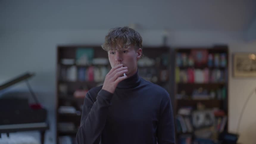A young man standing in a large living room with a cigarette in his mouth