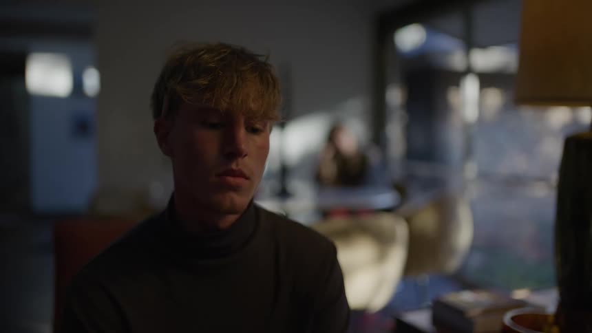 The face of a young man in a black shirt who is sitting looking forward in sad tones