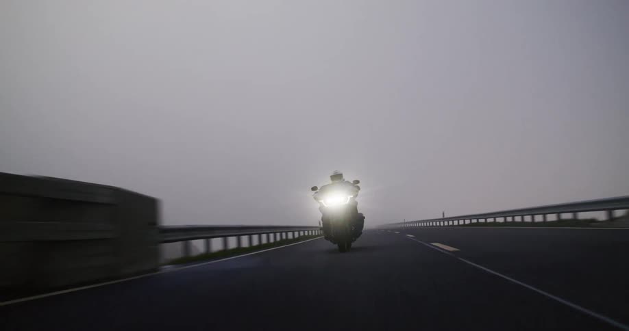 An adult rides a motorcycle through a tunnel on a foggy remote highway