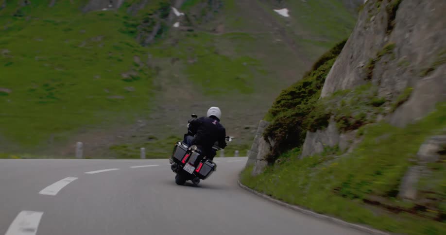 Motorcyclist rides a winding road surrounded by green mountains and rocks