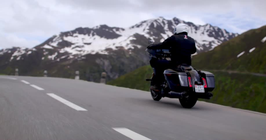 An adult rides a motorcycle on a high mountain road on a cloudy day