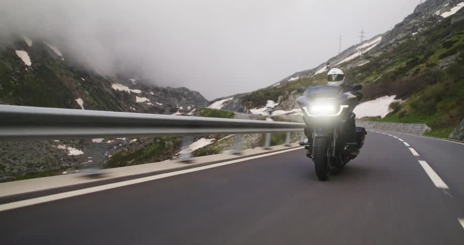 Motorcyclist in white helmet rides on mountain road surrounded by fog and snow