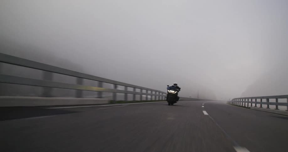 A motorcycle is driving on the winding road in the fog