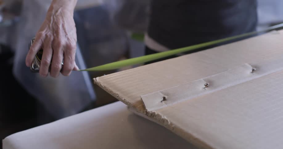 A man is measuring a piece of cardboard with a measuring tape