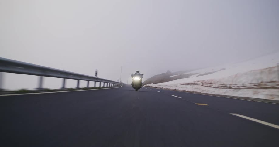 Motorcyclist rides a winding road surrounded by snow and shrouded in dense fog