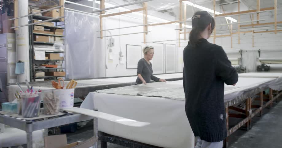 An older woman gives a younger woman a clipboard while they work in a textile factory