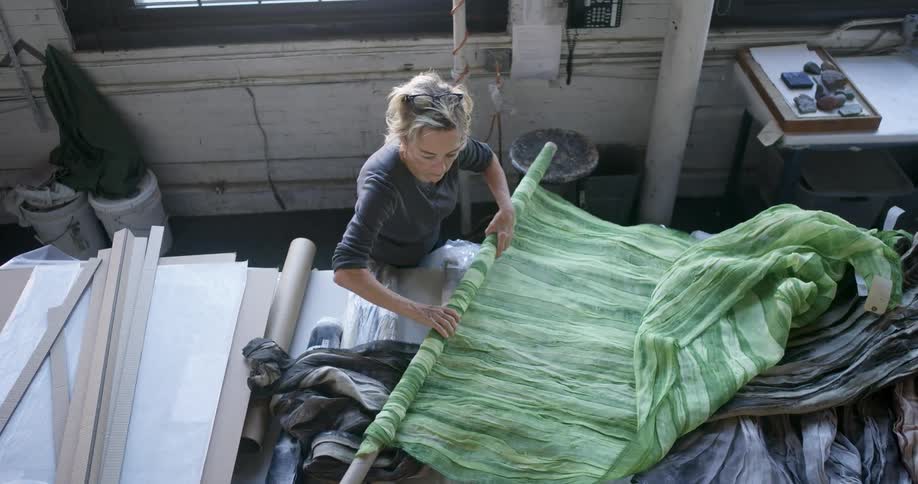 A blonde woman is folding a green fabric using her hands