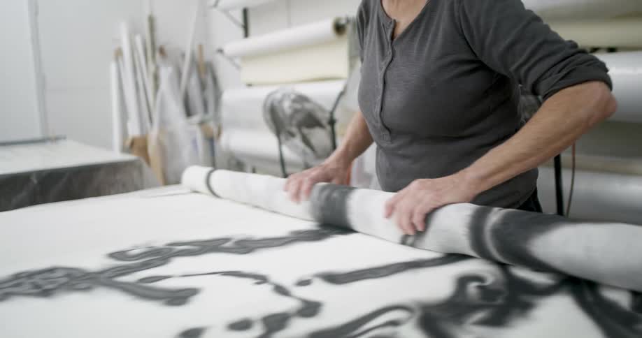 Woman carefully rolls a large white fabric on a work table in a studio