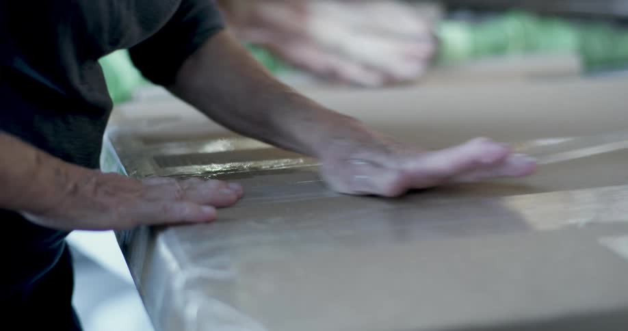 A man places tape on a large thin cardboard box