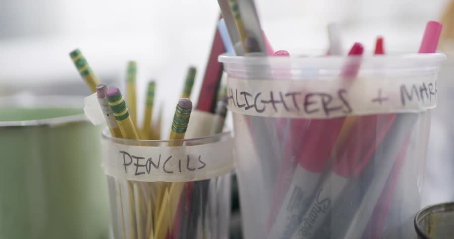 Labeled plastic cups store yellow pencils with green erasers and colored markers