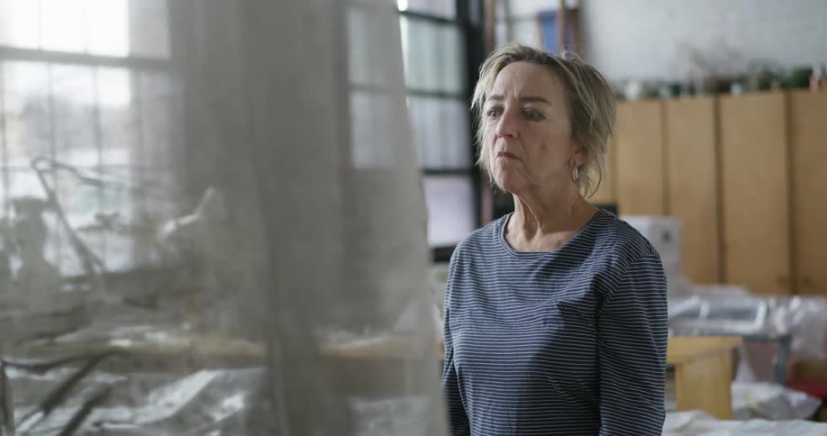 Thoughtful woman looks at a translucent fabric inside a brightly lit art studio