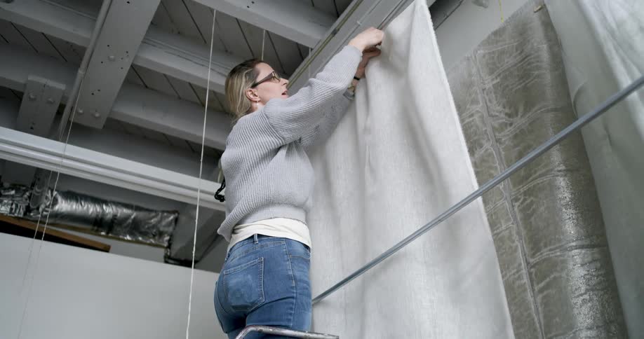 Woman on a ladder adjusting a white fabric curtain