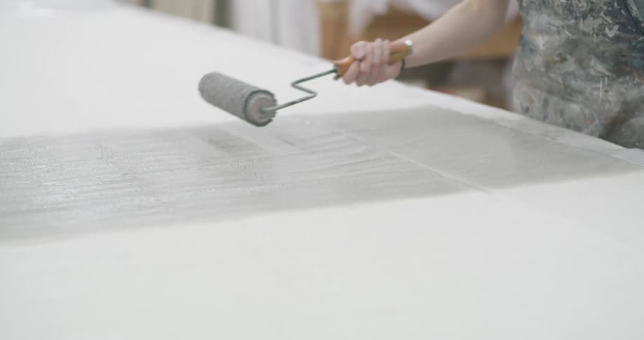 Person uses a roller to apply an even layer of paint to a large stretched fabric