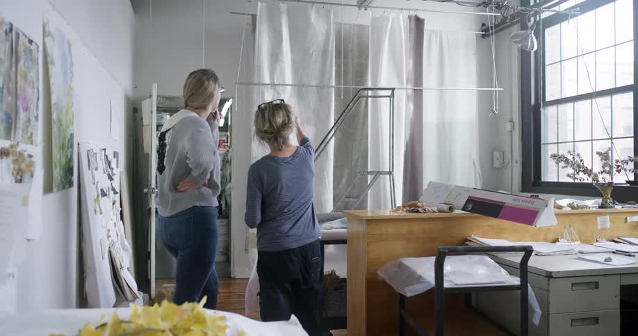 Two women are talking and pointing at hanging fabric